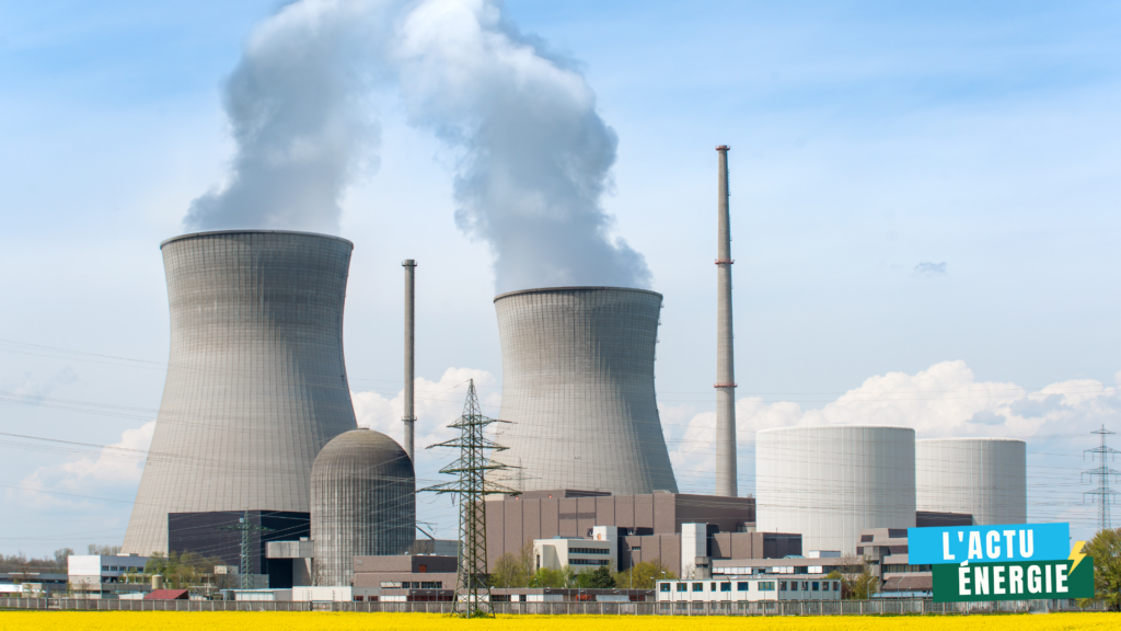 Une centrale nucléaire avec deux grandes tours de refroidissement émettant de la vapeur d'eau dans le ciel. Plusieurs bâtiments industriels et cheminées sont visibles autour, avec des lignes électriques à haute tension traversant l’image. À l'avant-plan, un champ de colza en fleurs contraste avec l'infrastructure industrielle.